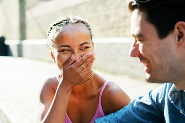 Mulher negra escondendo a boca rindo enquanto olha para um homem