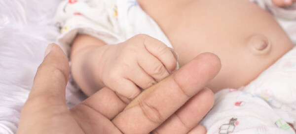 Bebê com hérnia umbilical segurando o dedo do cuidador