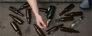 Homem deitado em sofá com garrafas de bebida alcoólica no chão ao lado