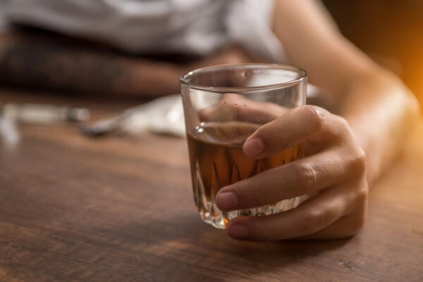 Pessoa segurando copo de bebida alcóolica em cima de mesa