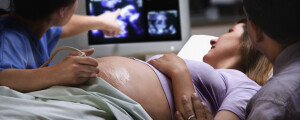 médica obstetra realizando ultrassom em mulher grávida, que está deitada em uma maca com um homem ao lado