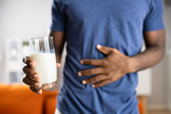 Homem de camiseta azul com a mão no estômago e segurando um copo de leite na outra mão