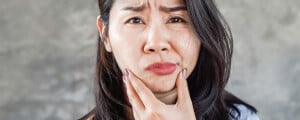 Mulher asiática com as mãos nas mandíbulas expressando desconforto