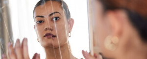 Mulher de cabelos presos olhando seu reflexo através de um espelho quebrado