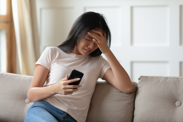 Mulher asiatica sentada no sofá olhandoc om cara de nojo para o celular