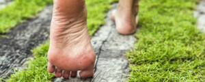 Pessoa caminhando com pés descalços sobre placas de madeira entremeadas à grama