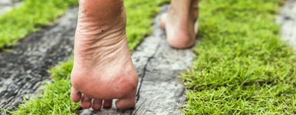 Pessoa caminhando com pés descalços sobre placas de madeira entremeadas à grama