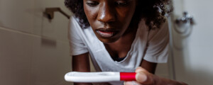 mulher grávida sentada em vaso sanitário no banheiro olhando para um teste de gravidez na mão