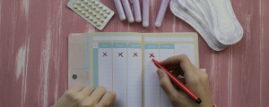Menina fazendo o controle do ciclo da menstruação em um caderno; imagem vista de cima.