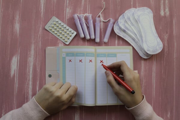 Menina fazendo o controle do ciclo da menstruação em um caderno; imagem vista de cima.