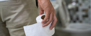 Homem segurando papel higiênico rumo ao vaso sanitário