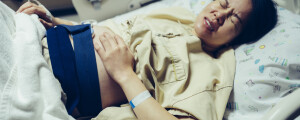 Mulher grávida deitada em maca de hospital com as mãos na barriga enquanto sente dor