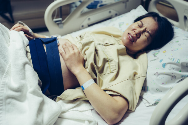 Mulher grávida deitada em maca de hospital com as mãos na barriga enquanto sente dor