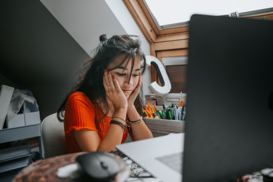 Adolescente sentada na frente de um computador sentindo estresse