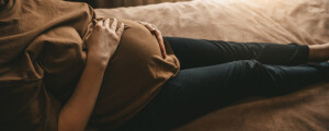 mulher grávida dentada na cama com as mãos na barriga