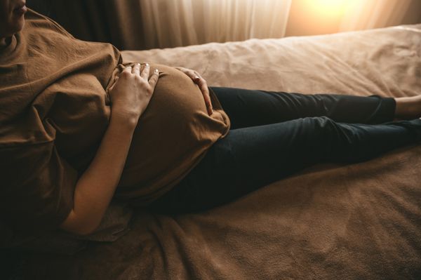 mulher grávida dentada na cama com as mãos na barriga