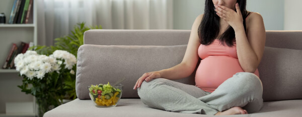 Mulher grávida passando mal com enjoos ao lado de uma tigela de salada