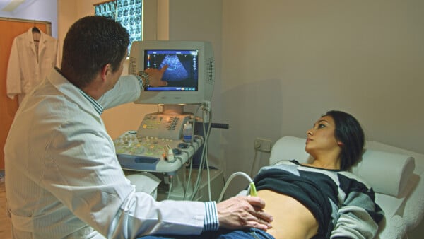 Mulher deitada em maca enquanto médico realiza ultrassom na barriga dela