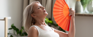 Mulher madura usando leque para se refrescar das ondas de calor da menopausa