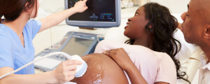 Mulher negra grávida fazendo ultrassonografia e médica apontando os detalhes em uma tela
