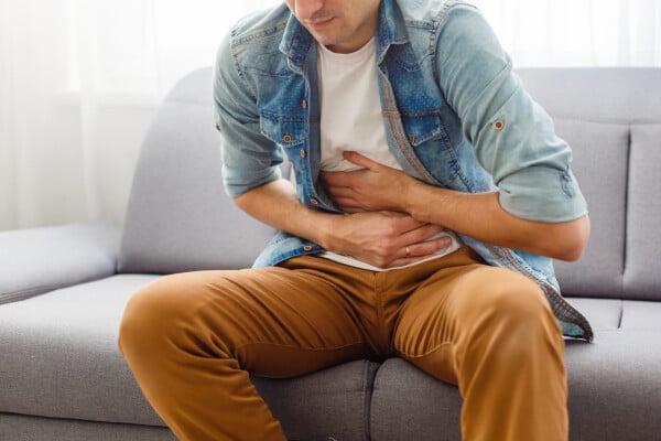 Homem branco sentindo dor no estômago sentado em um sofá