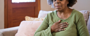 Mulher idosa sentada no sofá de sala com a mão no peito sentindo dor