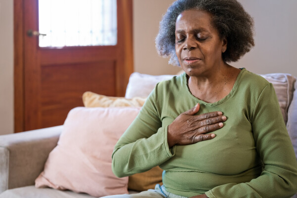 Mulher idosa sentada no sofá de sala com a mão no peito sentindo dor