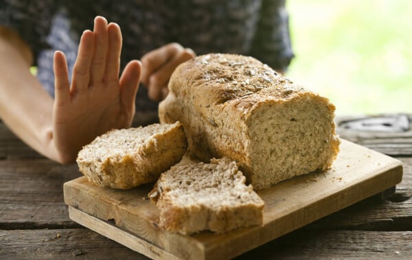 Close de uma mão em sinal de negação em frente a uma tabua com pães