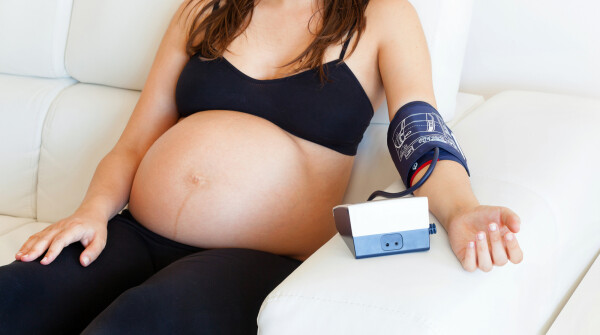 Mulher grávida sentada em sofá medindo a pressão