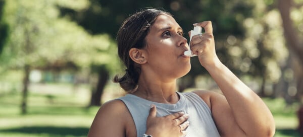 Mulher usando sua bombinha de asma durante treino ao ar livre