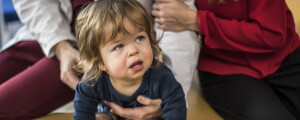 Bebê loiro sentado sendo em consulta médica segurado pelos pais