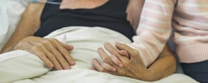 Pessoa com AVC deitada em maca de hospital com mulher segurando a mão dela
