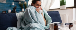 Mulher com doença do legionário sentada no sofá, com um cobertor ao redor do corpo, enquanto assoa o nariz