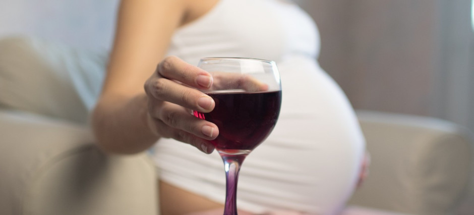 Mulher grávida segurando uma taça de vinho tinto.