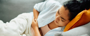 Mulher deitada no sofá com as mãos sobre a barriga, se contorcendo de cólica, um dos sintomas de endometriose profunda