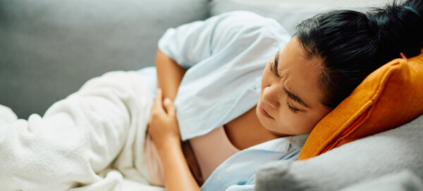 Mulher deitada no sofá com as mãos sobre a barriga, se contorcendo de cólica, um dos sintomas de endometriose profunda