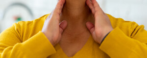 Mulher com a mão no pescoço, próximo a região da glândula tireóide