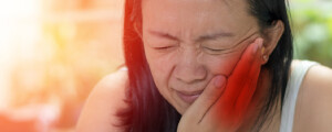 Mulher branca asiática com as mãos ao lado do rosto sinalizando dor na articulação temporomandibular