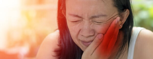 Mulher branca asiática com as mãos ao lado do rosto sinalizando dor na articulação temporomandibular
