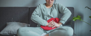 Mulher sentada em um sofá com uma bolsa térmica na região abdominal