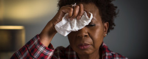 Mulher com gripe apoia a mão na testa enquanto segura um papel