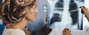 Mulher com câncer usando um lenço na cabeça olha um exame de raio X mostrado por um médico