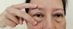 imagem aproximada dos olhos de uma mulher, com a mão erguida mostrando dois dedos na frente dos olhos