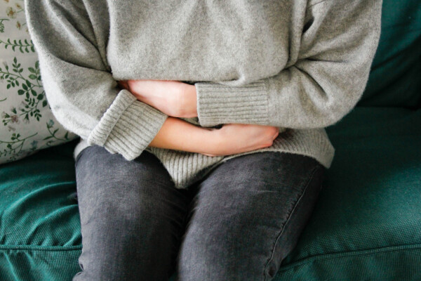 Mulher sentada no sofá abraçando o estômago