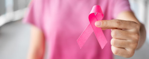 Foto aproximada de mulher segurando laço rosa, símbolo da conscientização acerca do câncer de mama