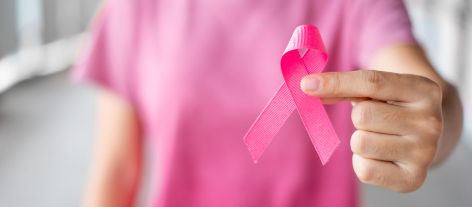 Foto aproximada de mulher segurando laço rosa, símbolo da conscientização acerca do câncer de mama