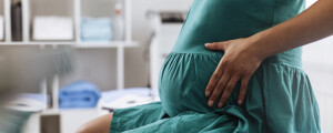 mulher grávida sentada em maca de consultório médico com as mãos sobre a barriga