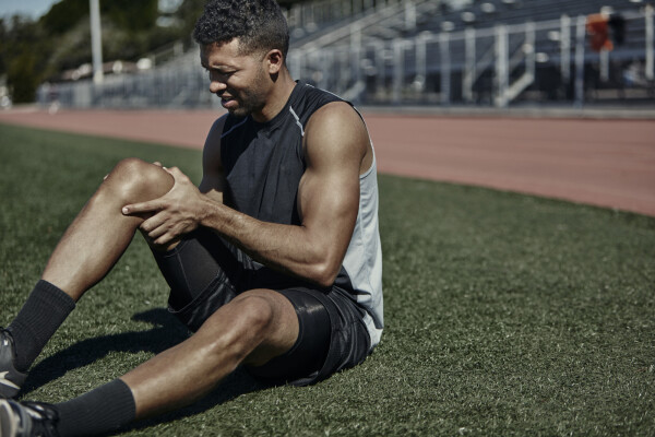 Homem sentando em um campo de atletismo com as mãos no joelho