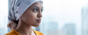 Mulher com leucemia utilizando um lenço na cabeça olhando pela janela