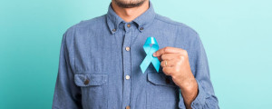 Homem com camisa jeans azul segura fita azul em frente ao peito.